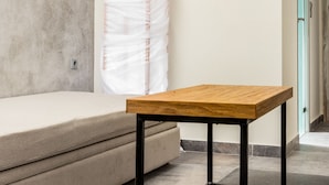 A room with a wooden table, a sofa, a concrete wall, and a teal door. - Lena Apartments (Thasos)