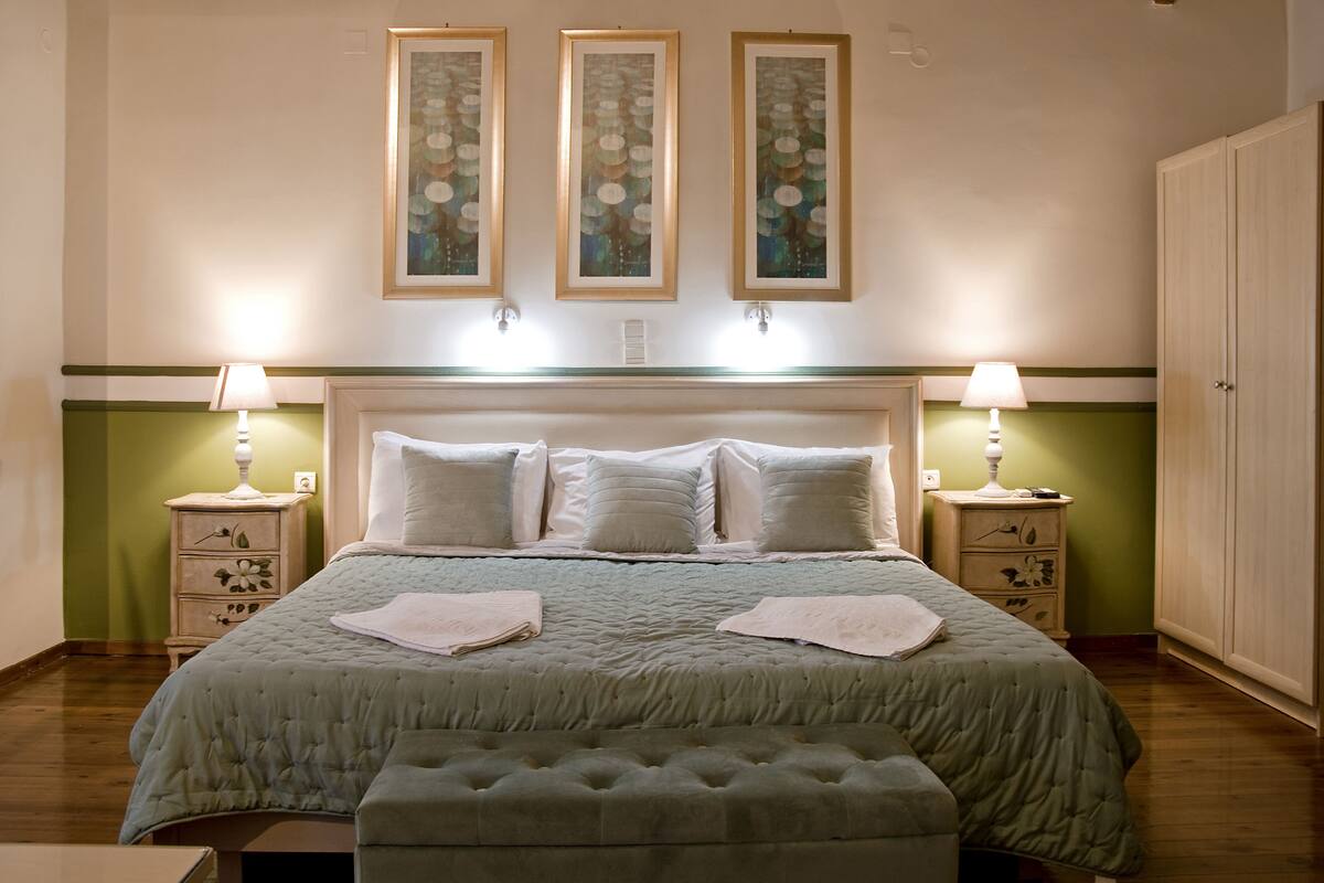 A neatly made bed with a green bedspread, two bedside tables with lamps, and three framed artworks on the wall.