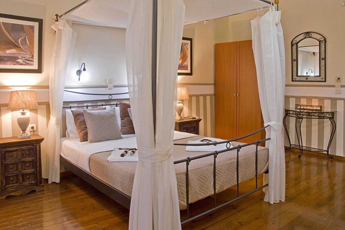 A four-poster canopy bed with a wooden headboard, bedside lamps, a wooden nightstand, and a mirror on the wall.