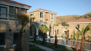 A stone building with a pool and palm trees. - Anemos Hotel (Gökçeada)