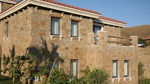 A stone building with a tiled roof, multiple windows, and a well-maintained garden with various plants. - Anemos Hotel (Gökçeada)
