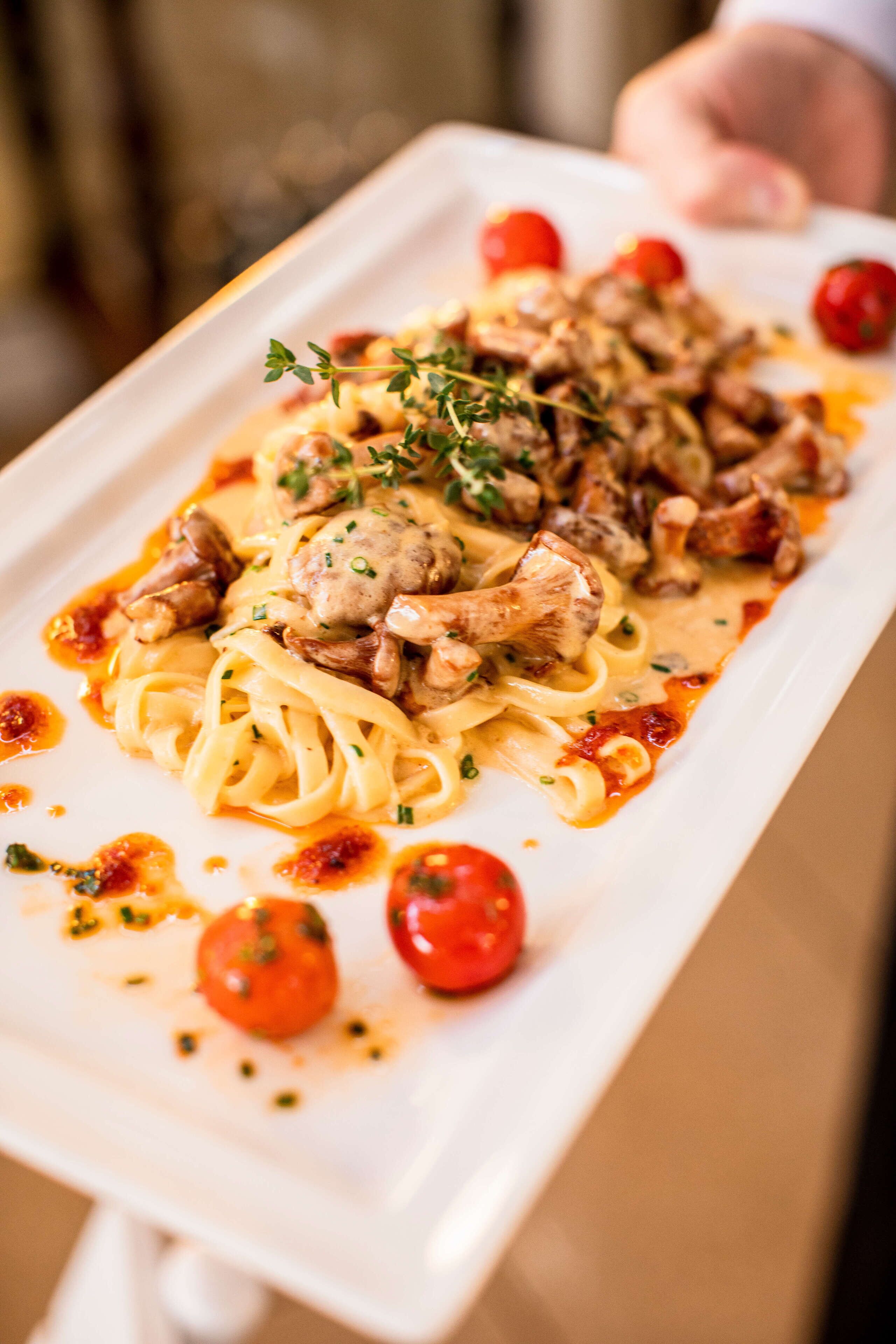 Un plato rectangular blanco con pasta, carne y tomates cherry adornados con hierbas.