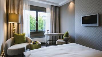 A hotel room with a bed, a round table, two chairs, a TV, and a window with curtains.