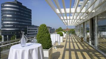 A rooftop terrace with tables set for dining, a view of a modern building, and a clear sky.