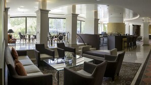 Eine Hotelhalle mit Rezeption, einer Sitzecke mit Sofas und Sesseln, einer Bar und einem gemusterten Teppich.
