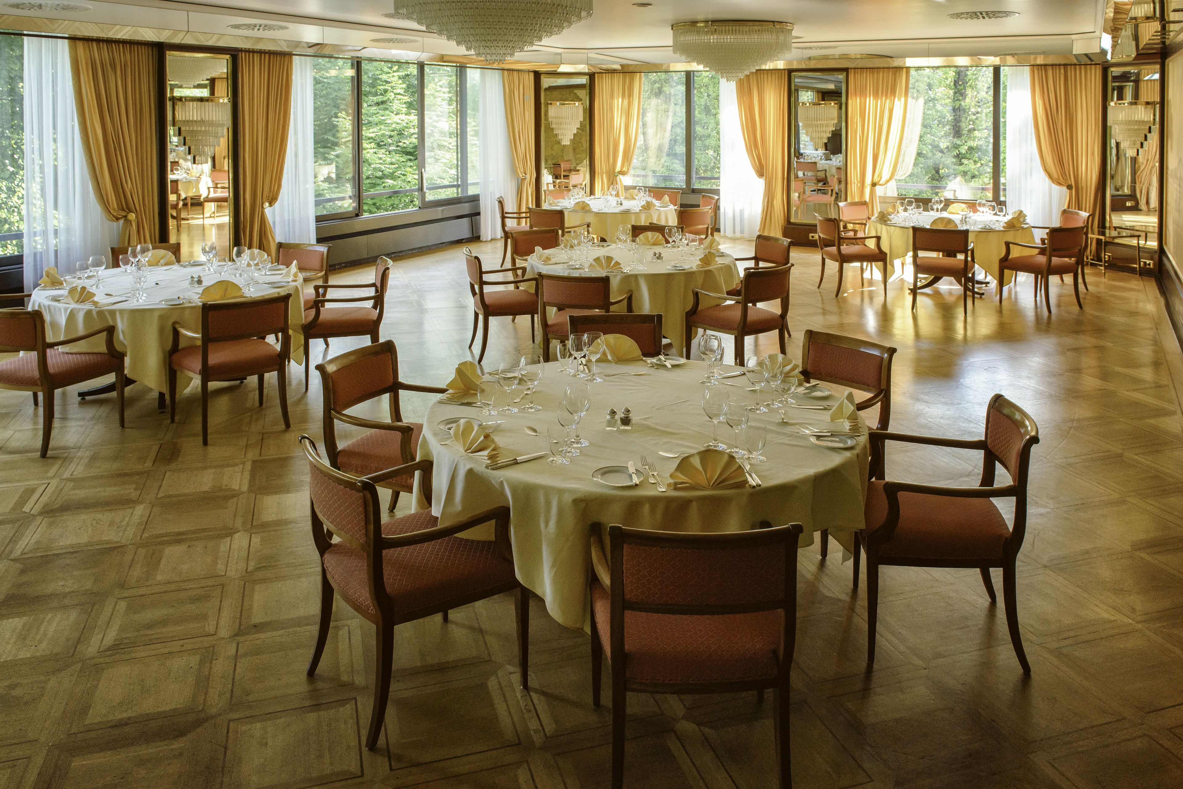 A spacious dining area with multiple round tables set for dining, surrounded by wooden chairs.