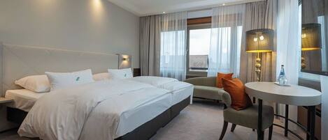 A hotel room with a large bed, a sofa, a small table, and a window with curtains.
