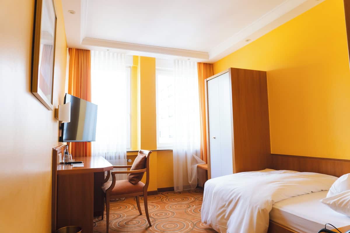 Quarto de hotel com cama, escrivaninha, cadeira, televisão e janela com cortinas.
