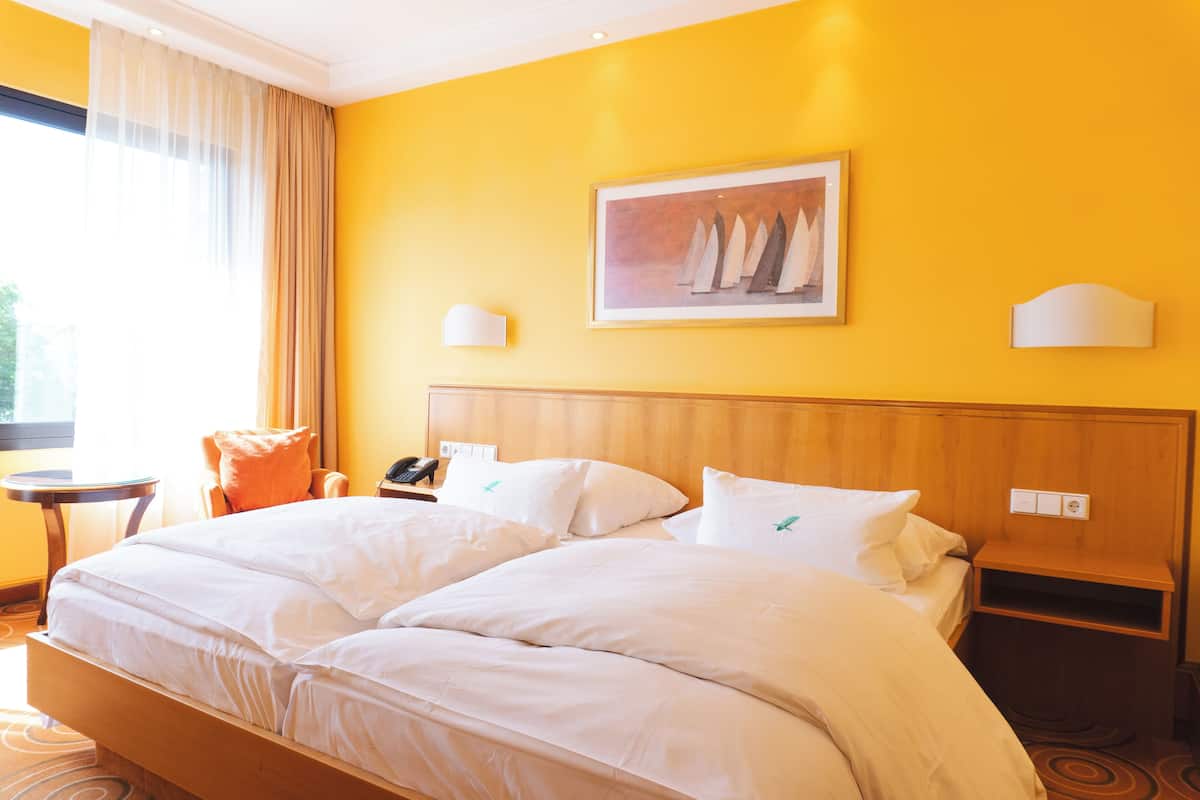 Uma cama de casal com lençóis brancos, cabeceira de madeira, mesa de cabeceira com telefone e um quadro de barcos à vela na parede.