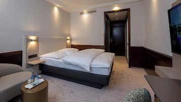 A modern hotel room with a large bed, bedside tables, a seating area, and a TV.