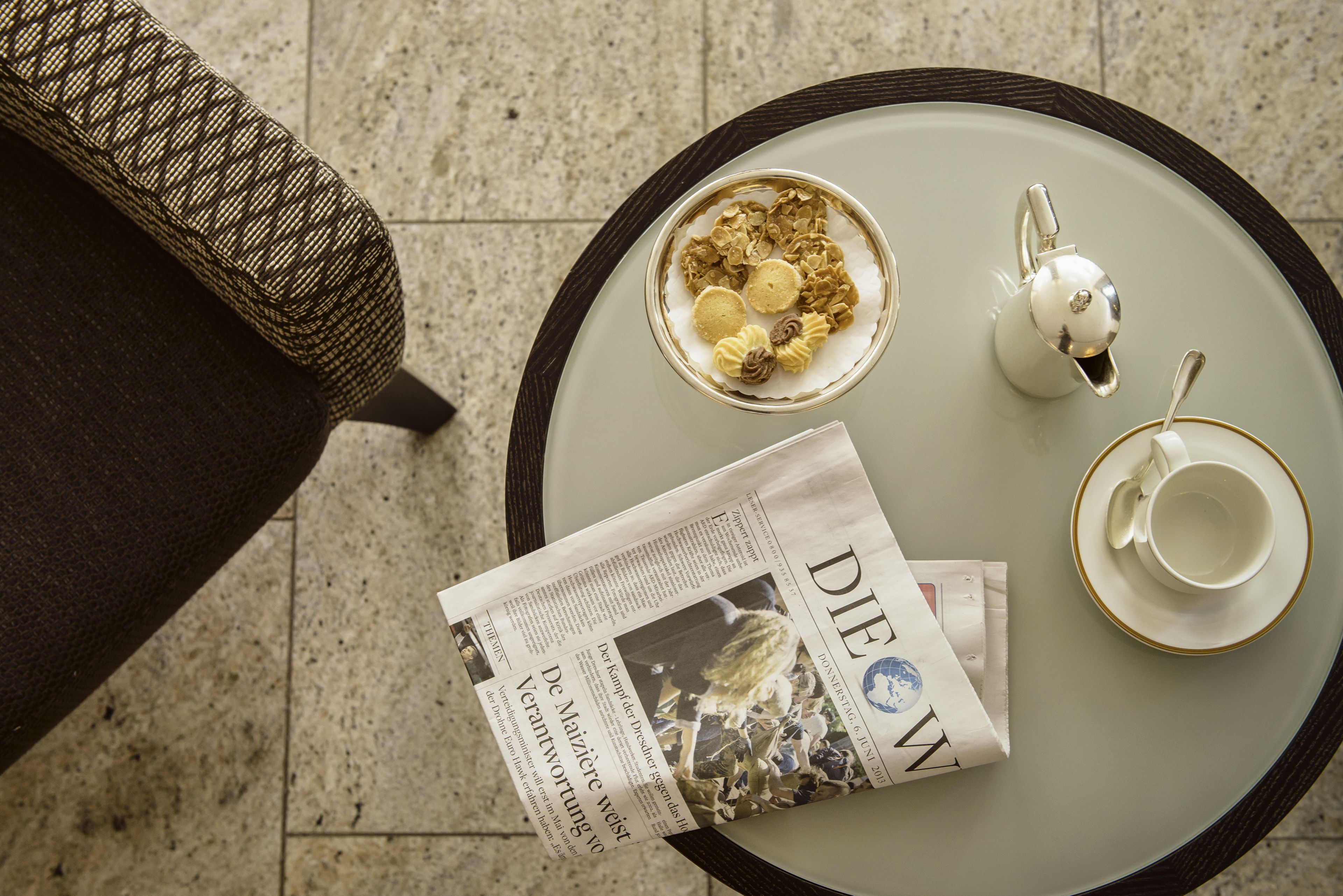 A table with a newspaper, a cup, a saucer, and a teapot.