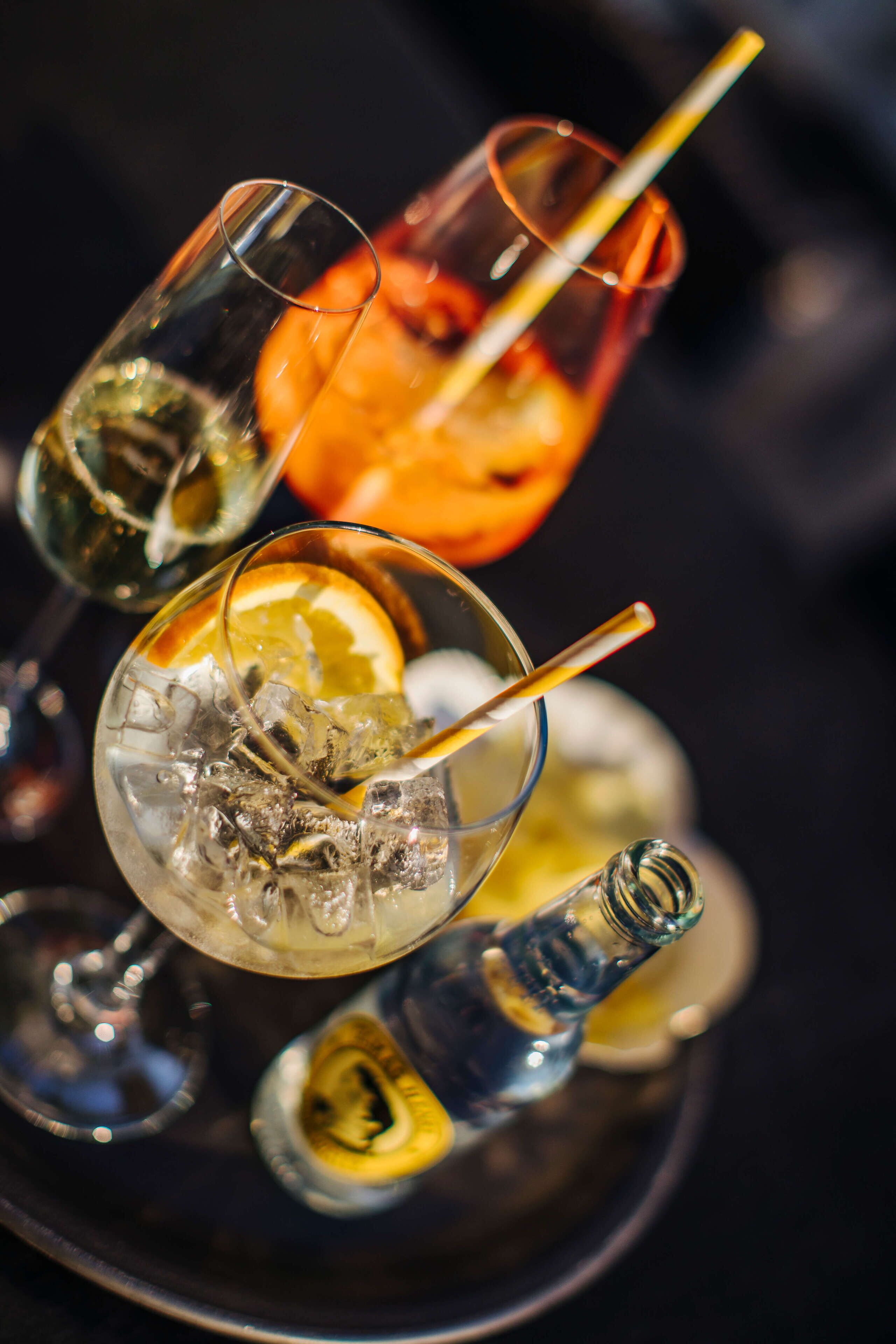 Three glasses of a beverage with ice cubes and a slice of orange, placed on a tray.