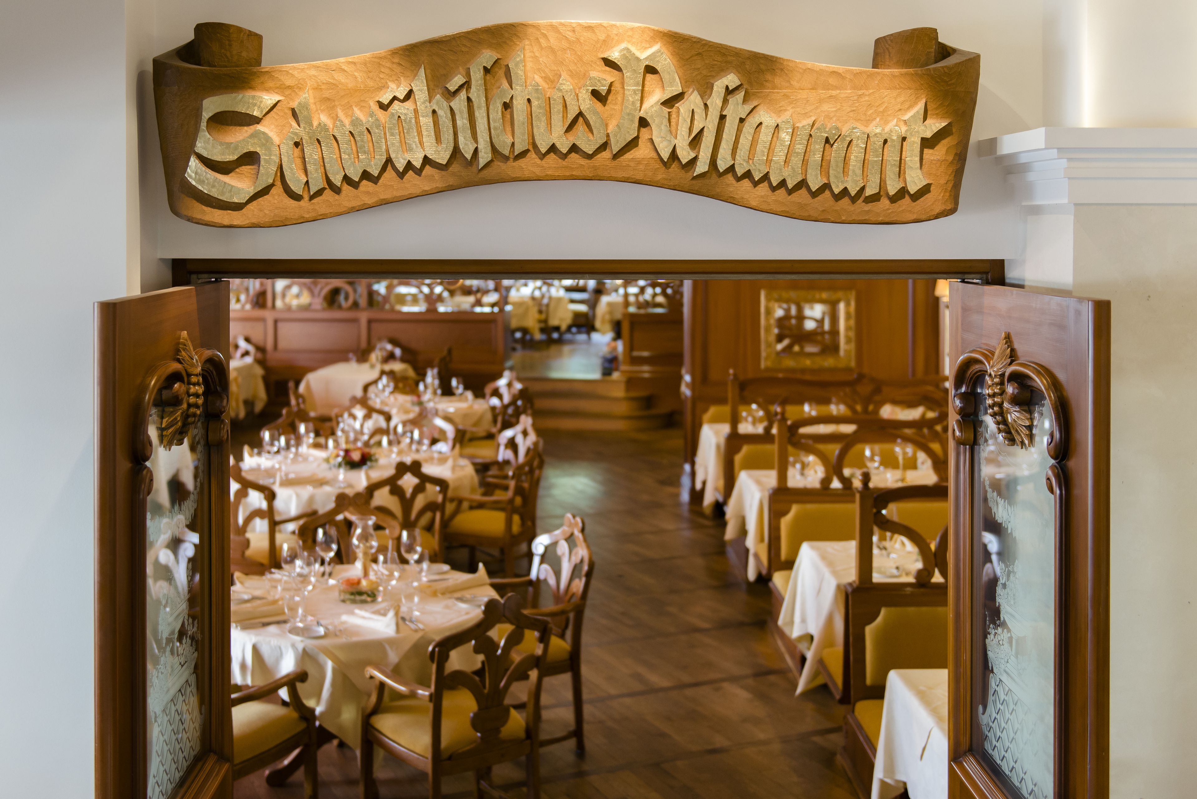 A restaurant interior with wooden decor, tables set with white tablecloths, and a sign reading "Schwabichs Restaurant".