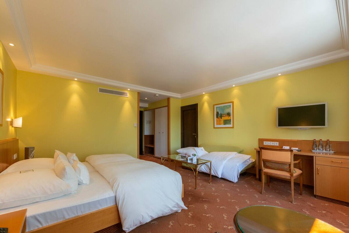 Quarto de hotel com duas camas, uma escrivaninha, uma cadeira, uma televisão e uma mesinha.