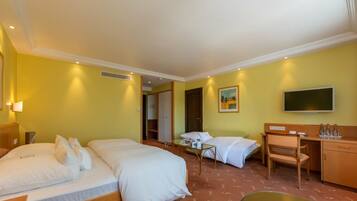 Quarto de hotel com duas camas, uma escrivaninha, uma cadeira, uma televisão e uma mesinha.