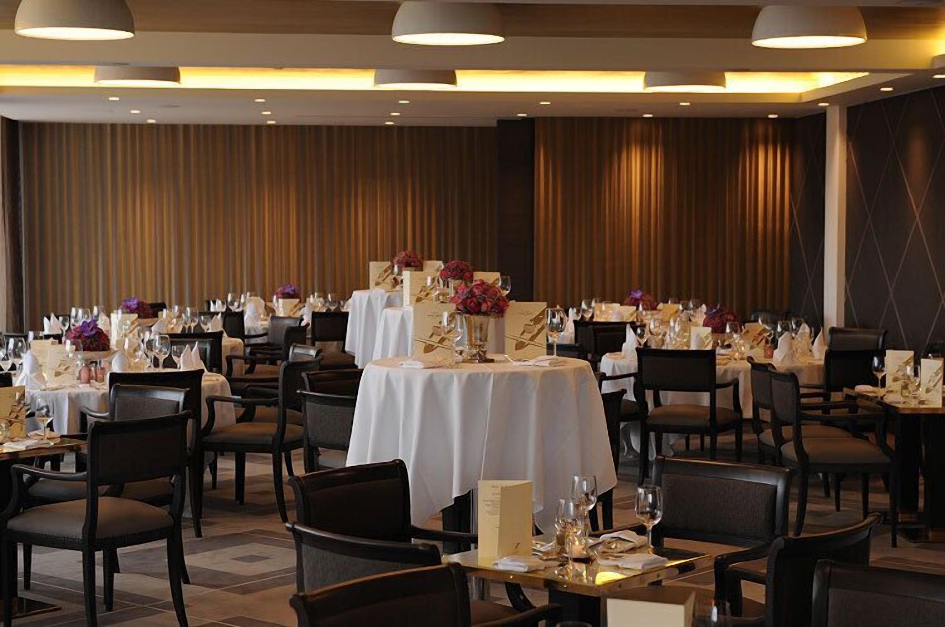 A dining area with multiple round tables set for guests, each with white tablecloths and centerpieces.
