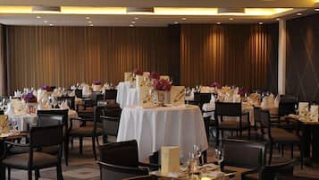 A dining area with multiple round tables set for guests, each with white tablecloths and centerpieces.