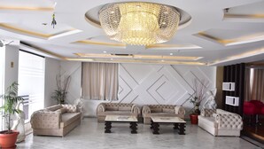 A modern living room with a chandelier, sofas, and potted plants. - Ishanika Hotel (Lucknow)