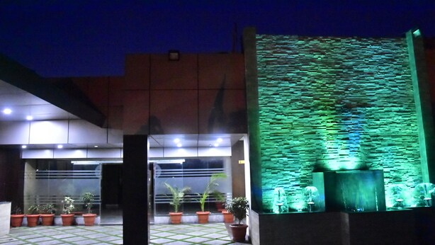 A building entrance with a tiled floor, potted plants, and a green-lit wall feature. - Ishanika Hotel (Lucknow)