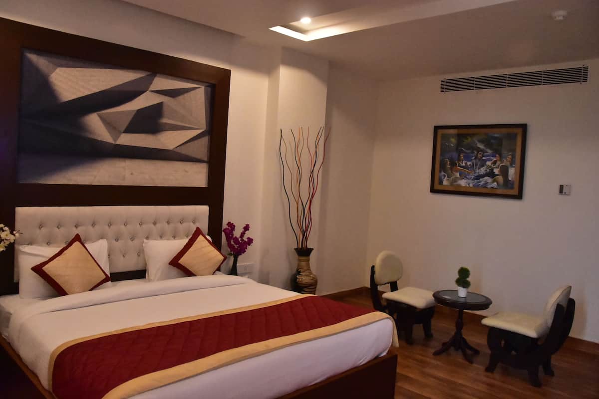 A bedroom with a large bed, a small table, two chairs, a painting, and a decorative wall piece.