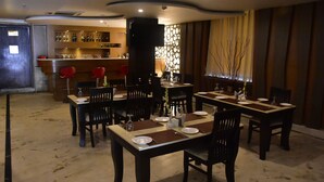 A restaurant with multiple dining tables set for guests, a bar area with bottles and glasses, and a decorative partition with branches. - Ishanika Hotel (Lucknow)