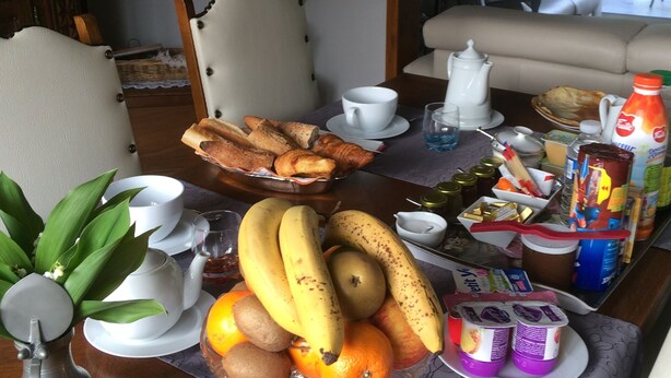 Een ontbijttafel met fruit, gebak en drankjes, een bank en een spiegel in een woonkamer.