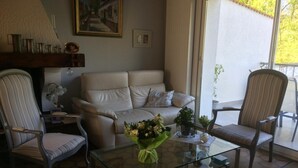 Een woonkamer met een beige bank, twee fauteuils, een glazen bijzettafeltje met bloemen, en een schilderij aan de muur.