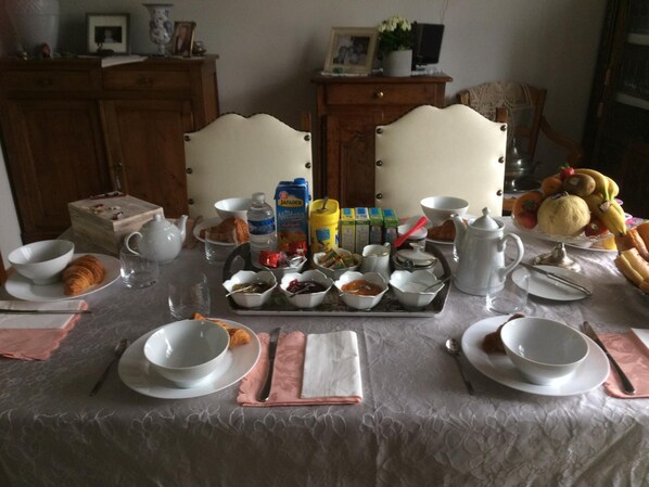 A breakfast table set with plates, bowls, a teapot, a jug, and a tray with various food items.