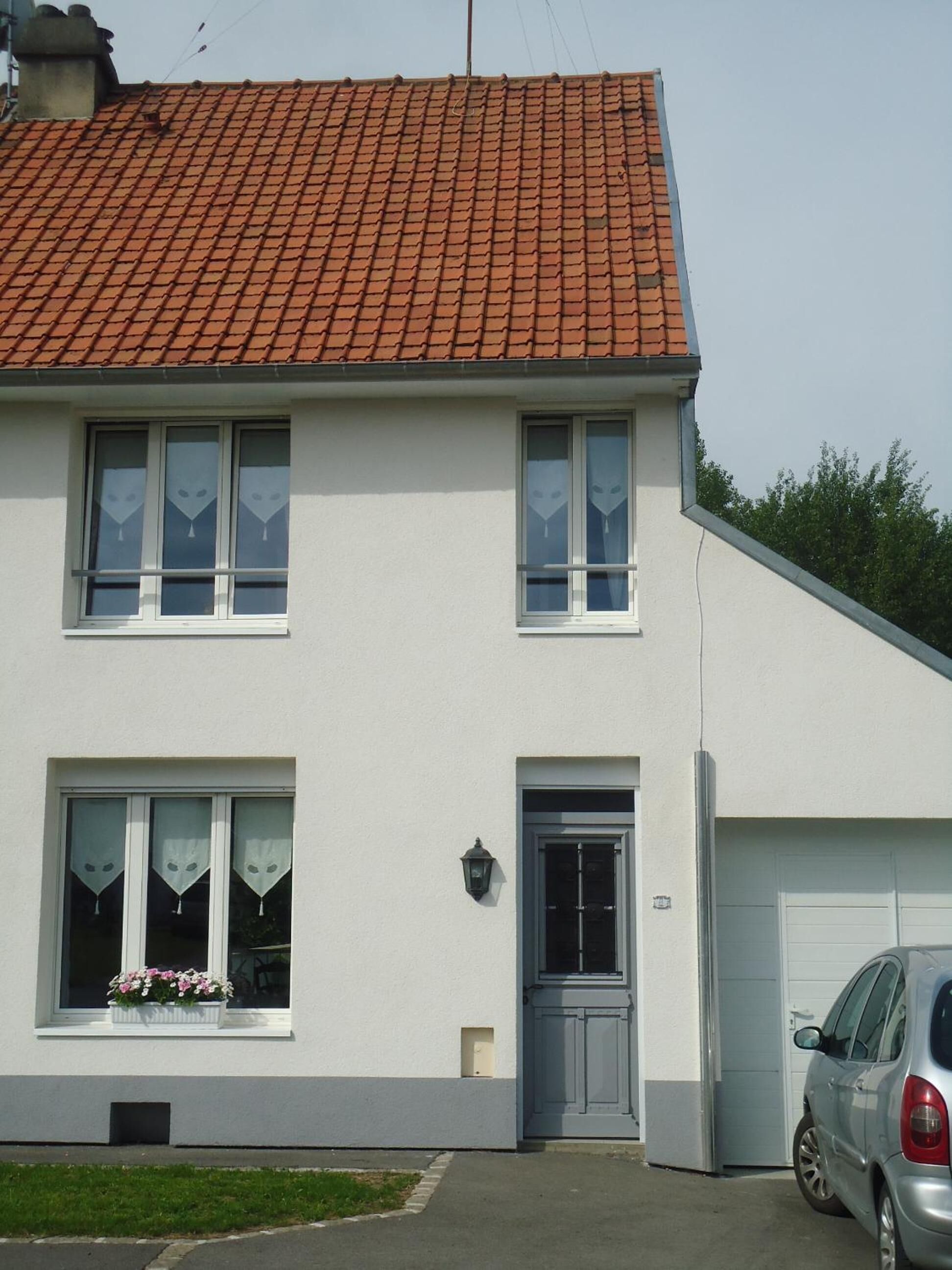 A two-story house with a red-tiled roof, white exterior walls, and a grey front door. There is a car parked in the driveway.