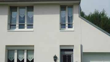 A two-story house with a red-tiled roof, white exterior walls, and a grey front door. There is a car parked in the driveway.