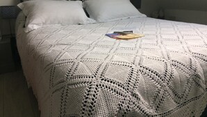 Een opgemaakt bed met een witte gebreide deken en twee kussens.