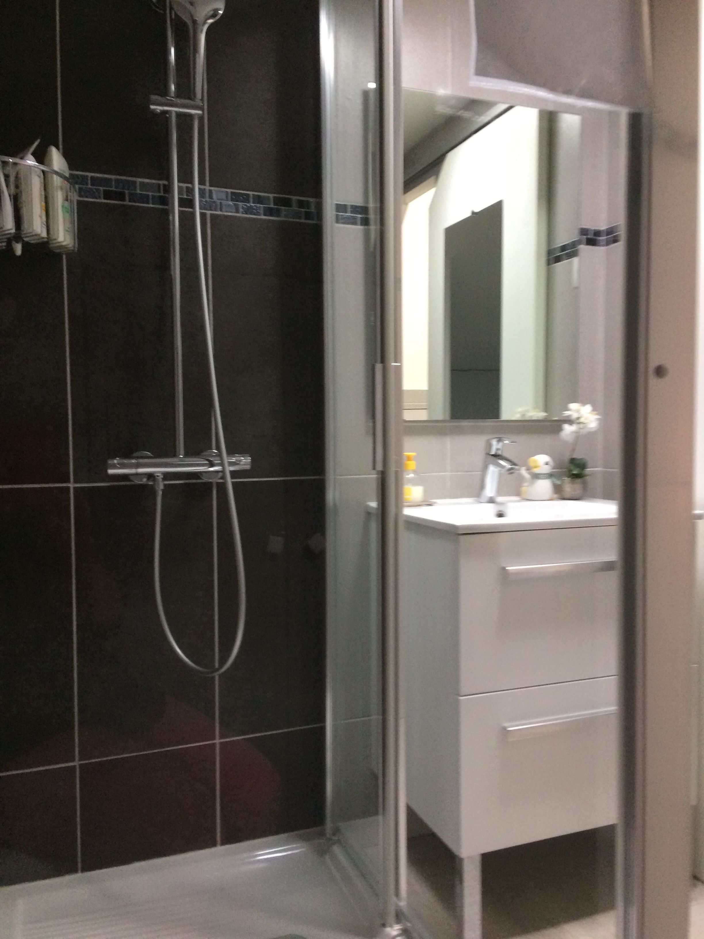 Un baño moderno con cabina de ducha de vidrio, un lavabo blanco con espejo y un revestimiento de azulejos.