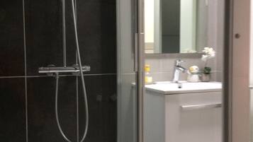 A modern bathroom with a glass shower enclosure, a white sink with a mirror, and a tiled backsplash.