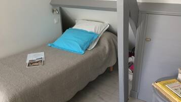 Een kleine eenpersoonskamer met een grijs plafond, een witte deur en een klein tafeltje met boeken.