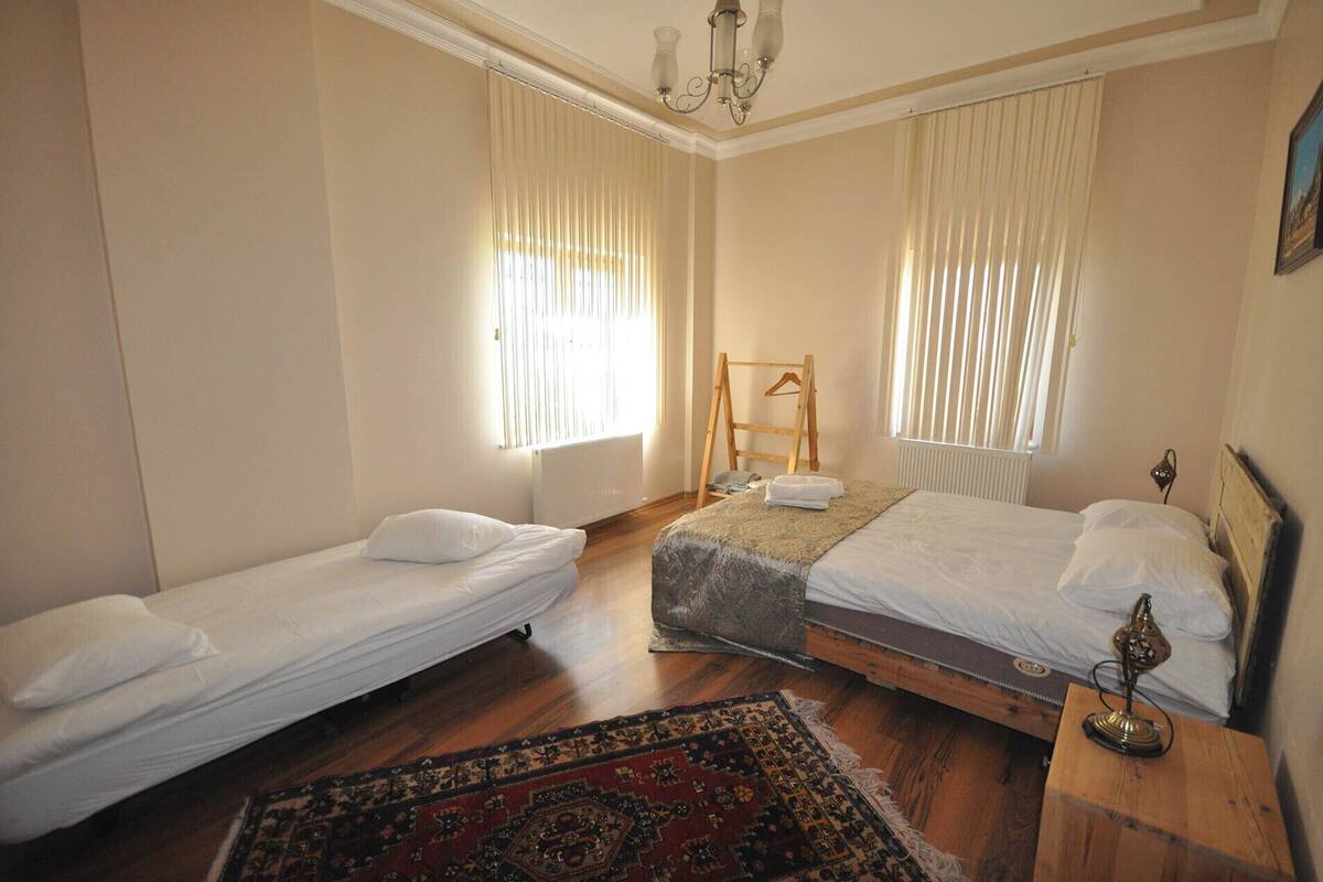 A room with two single beds, a wooden dresser, a small table with a lamp, and a radiator.