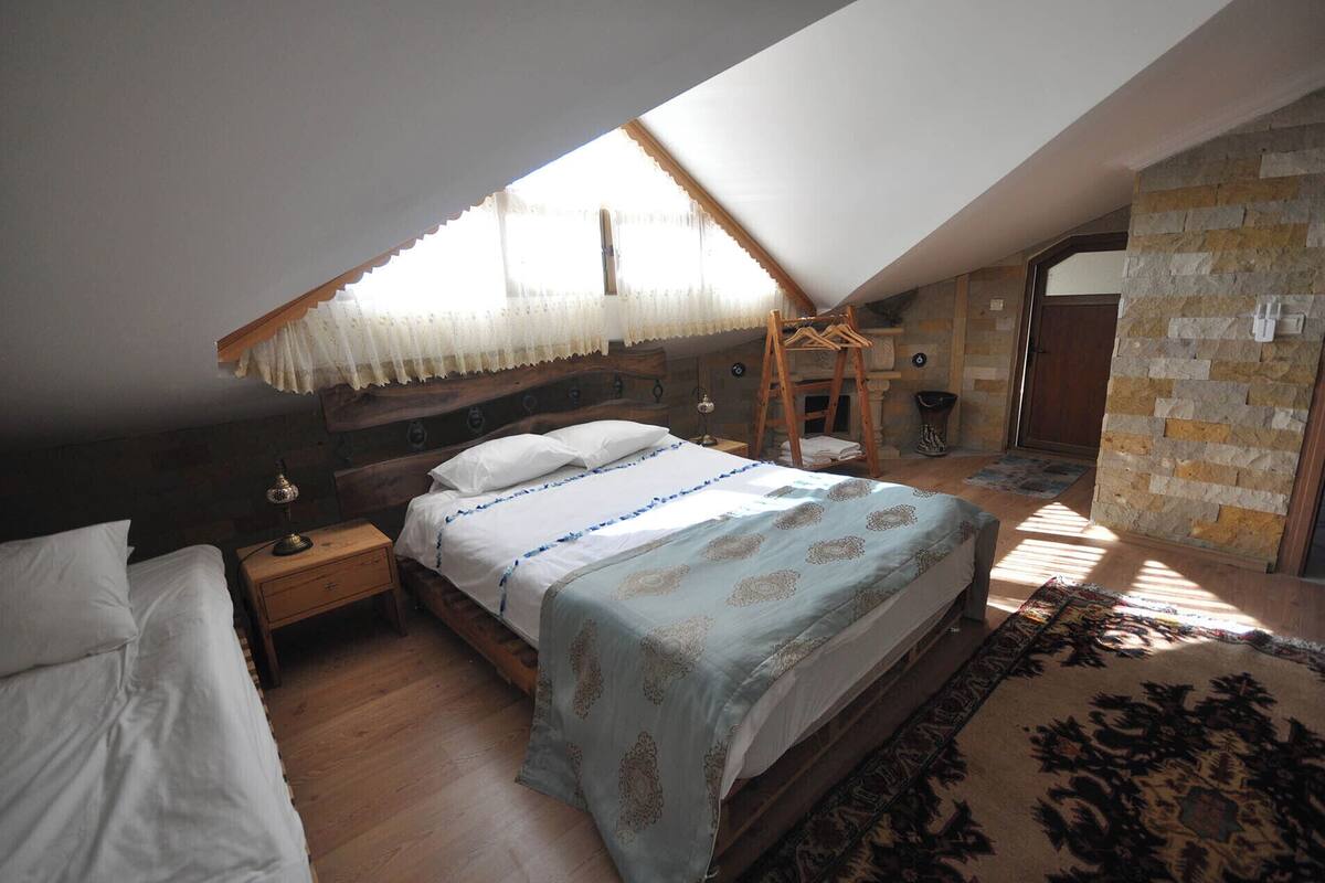 A bedroom with a sloped ceiling, a wooden bed, a nightstand, a hanging clothes rack, and a stone wall.