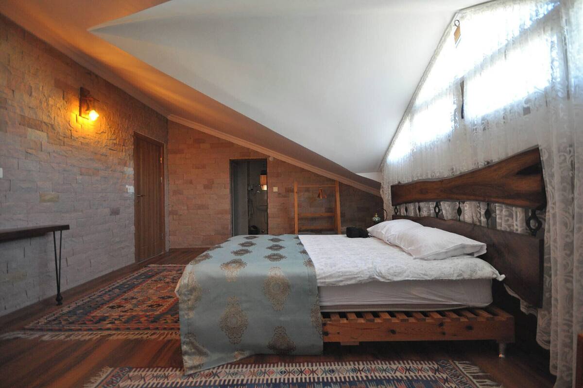A bedroom with a wooden bed, a patterned rug, and a brick wall with a light fixture.