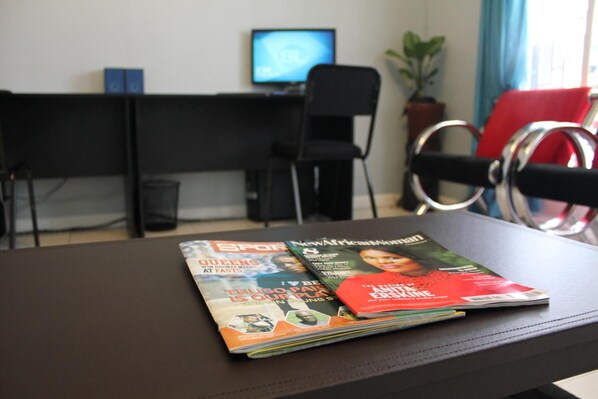 A desk with a computer monitor, a chair, a magazine, and a potted plant. - Blue Lagoon Lodge Blantyre (Blantyre)