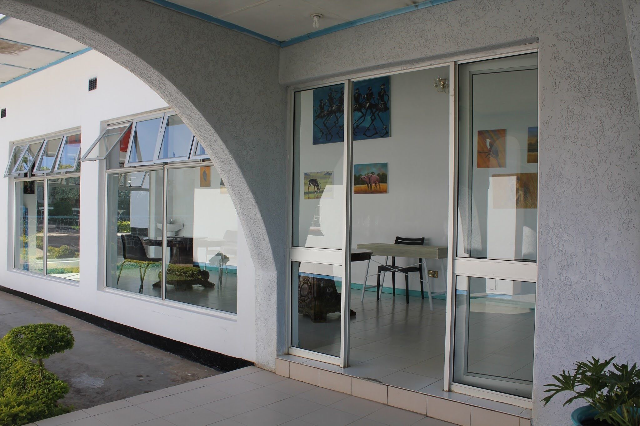 A modern building with large glass windows, a covered outdoor area with a table and chairs, and a potted plant.