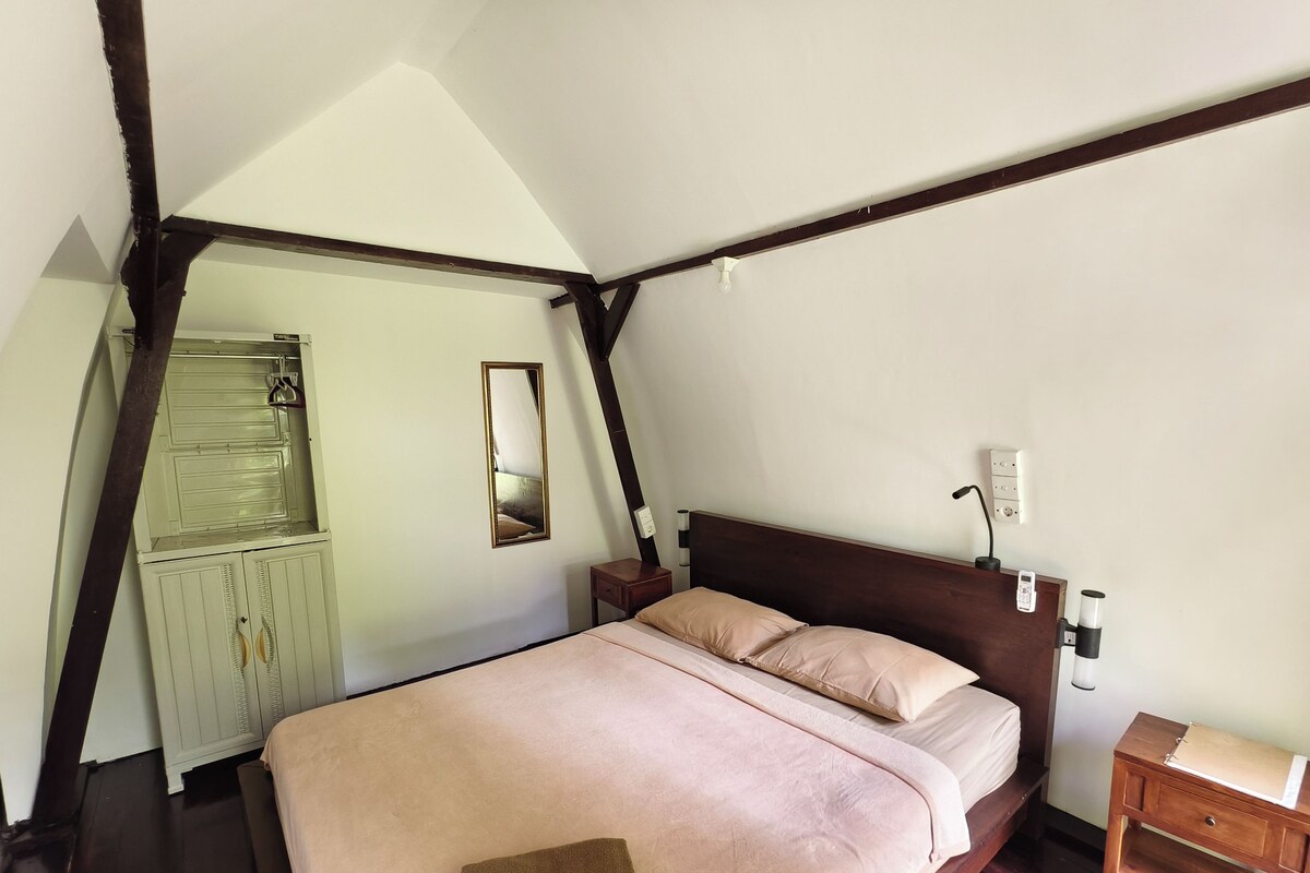 A bedroom with a wooden headboard, a bed with beige bedding, a bedside table with a lamp, and a wardrobe.