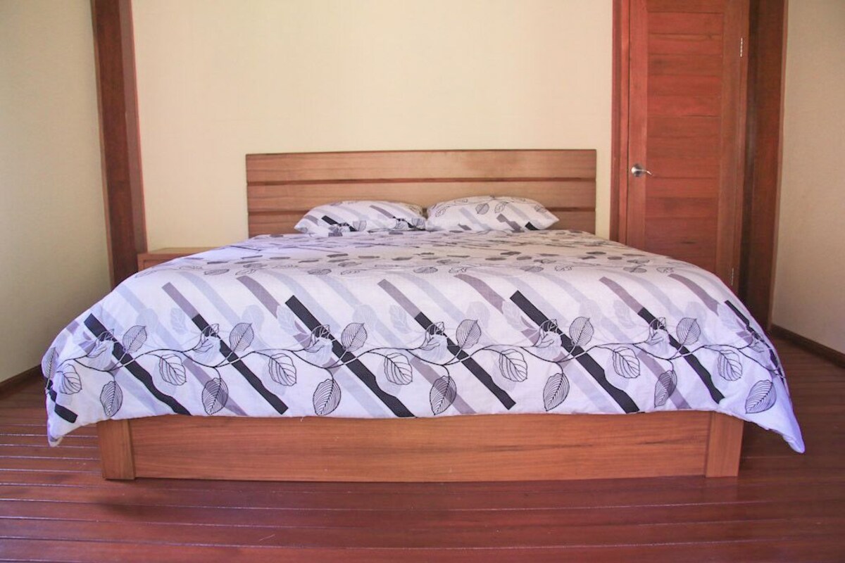A single bed with a patterned bedspread and wooden headboard in a room with wooden flooring and a wooden door.