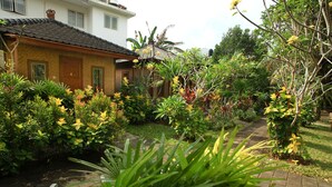 A house with a tiled roof, surrounded by lush greenery and flowering plants. - Timbis Homestay Bali (Kutuh)