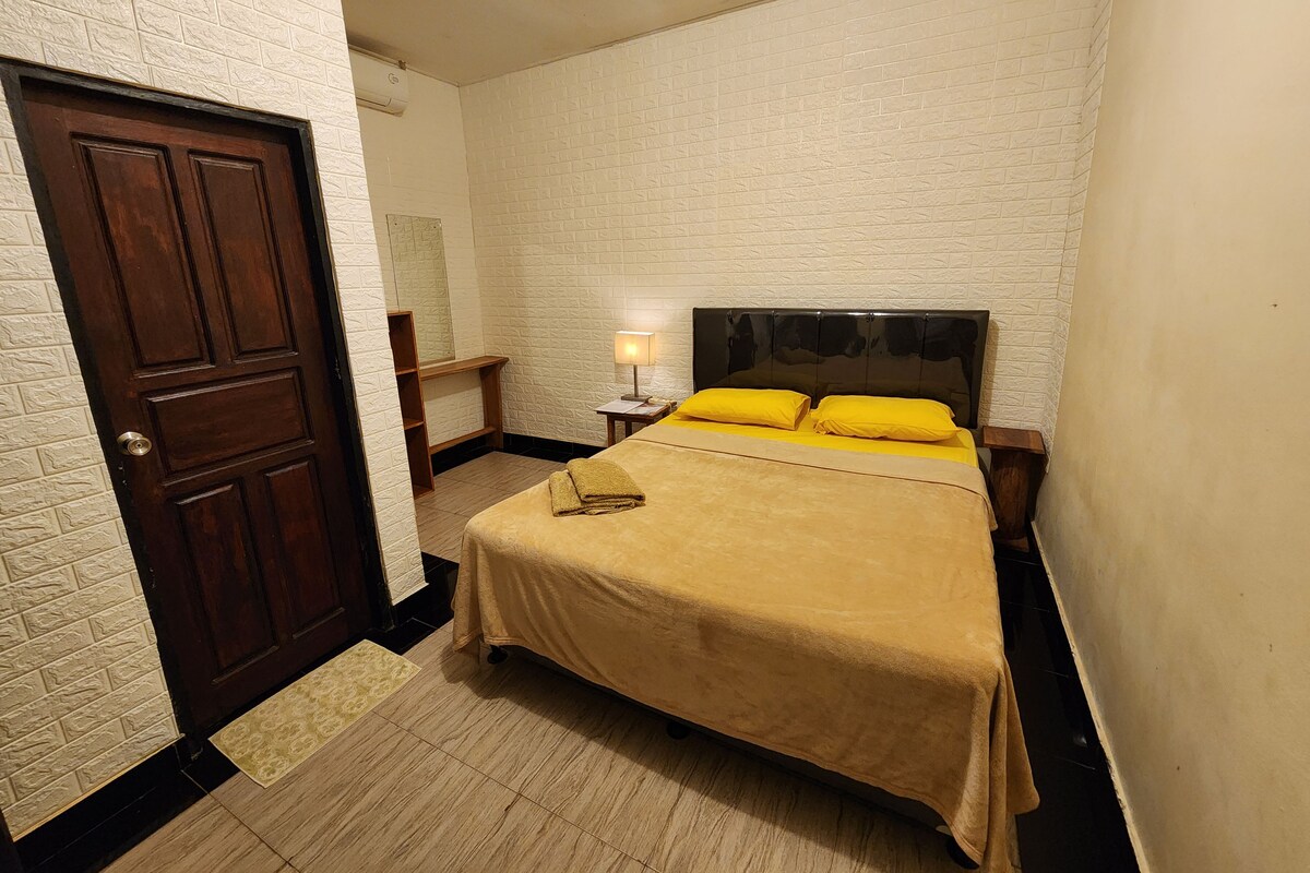 A bedroom with a bed, a nightstand, a lamp, and a door.