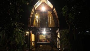 A wooden structure with a triangular roof and a balcony, surrounded by dense foliage. - Timbis Homestay Bali (Kutuh)