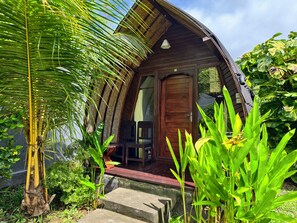 A wooden structure with a curved roof, a wooden door, and a small porch area. - Timbis Homestay Bali (Kutuh)