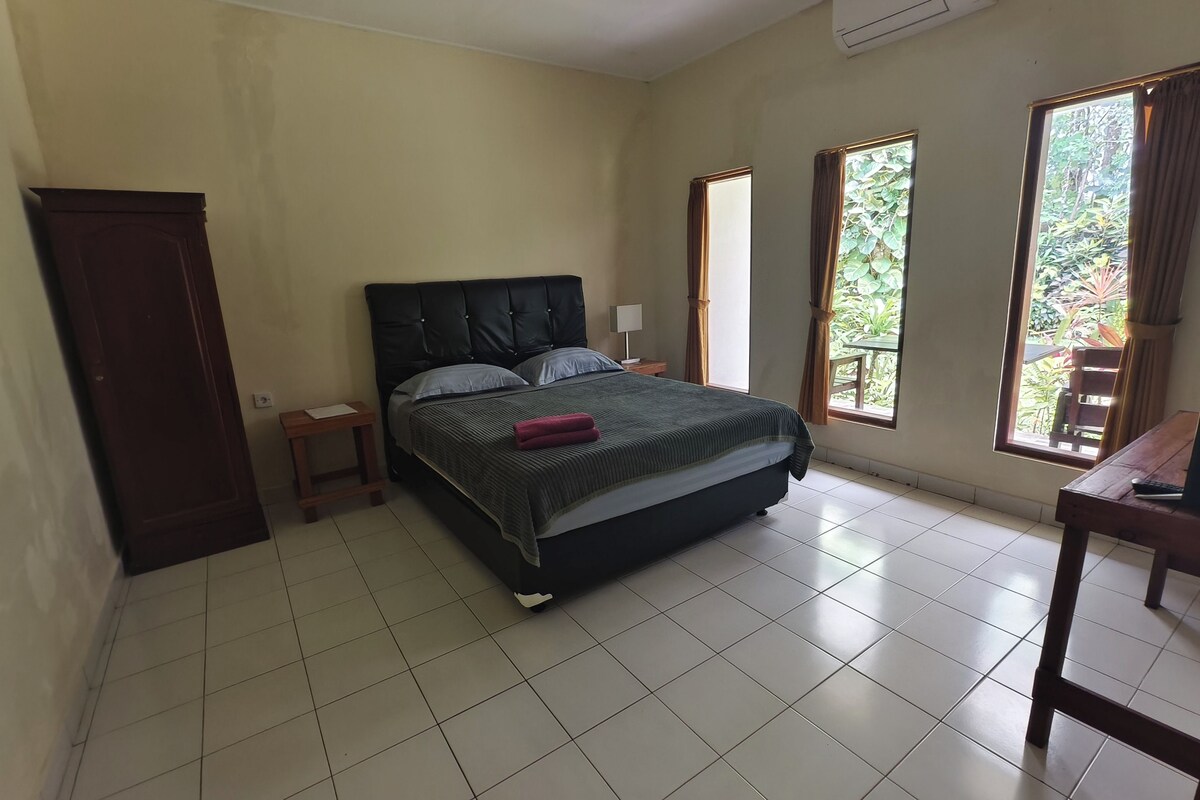 A bedroom with a bed, a nightstand, a desk, and large windows.