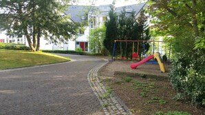 A paved pathway leading to a playground with a red slide and a yellow swing set. - Hotel Nümbrecht (Nümbrecht)