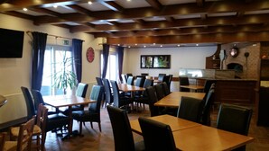A restaurant with wooden tables and chairs, a brick wall with a fireplace, and a clock on the wall. - Hotel Nümbrecht (Nümbrecht)