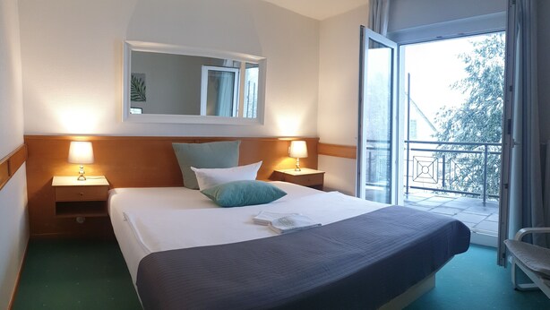 A hotel room with a large bed, two bedside tables with lamps, a window with a view of trees, and a balcony. - Hotel Nümbrecht (Nümbrecht)