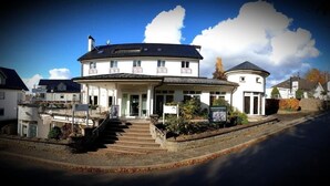 A two-story building with a central entrance, a covered porch, and a circular extension. - Hotel Nümbrecht (Nümbrecht)